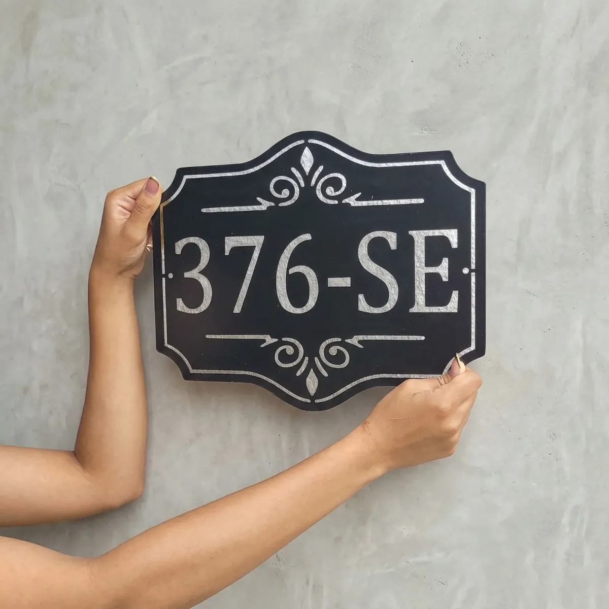 Placa de número residencial sendo posicionada na parede, mostrando a escala real da peça